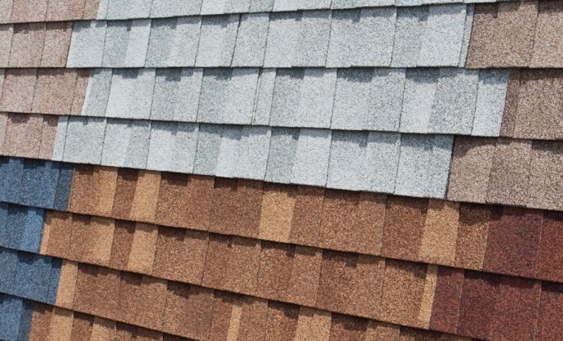 Close-up of a roof showing a gradient of asphalt shingle colors, from cool gray to warm brown.