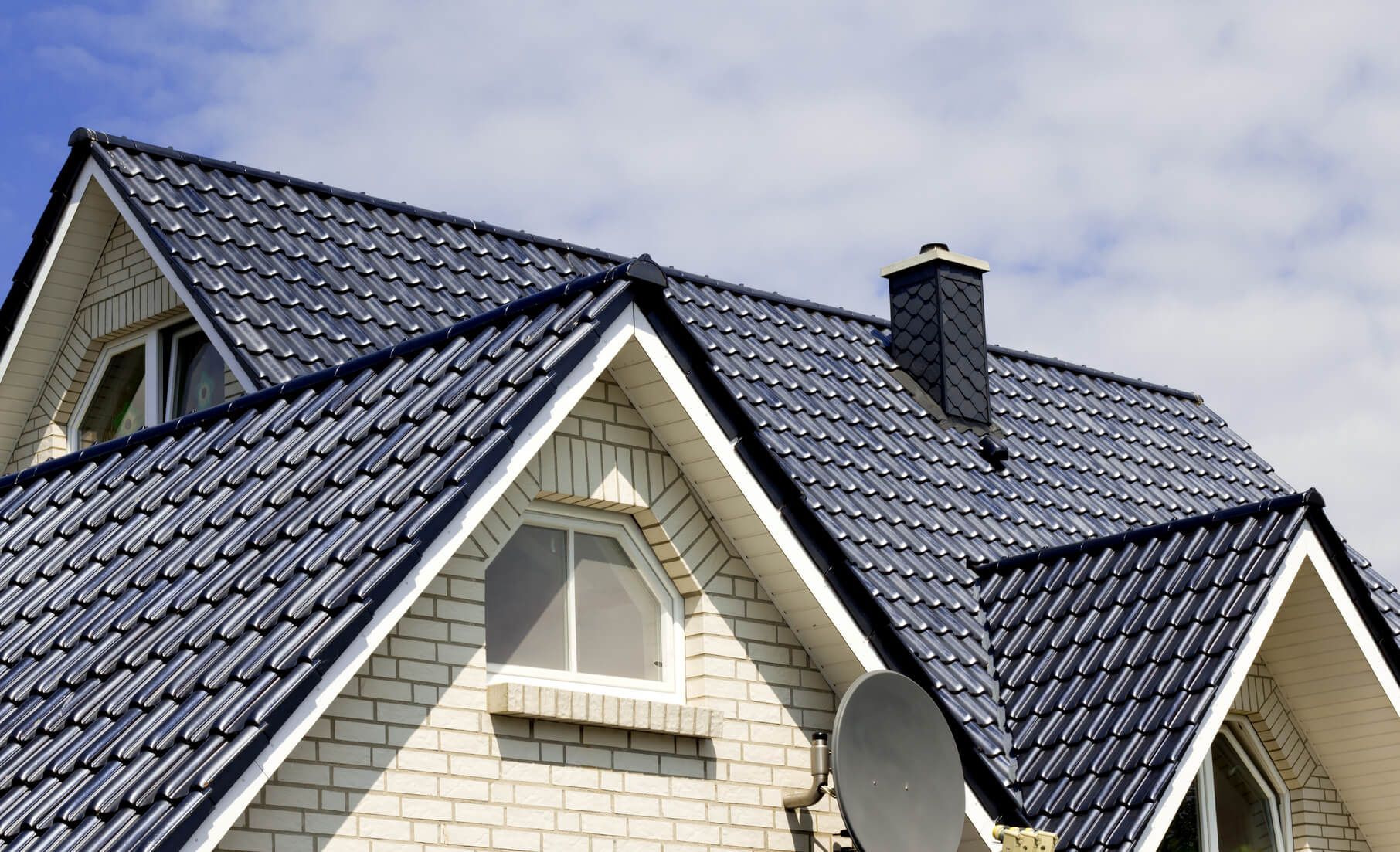 House with a dark blue tiled roof, chimney, satellite dish, and white brick exterior.