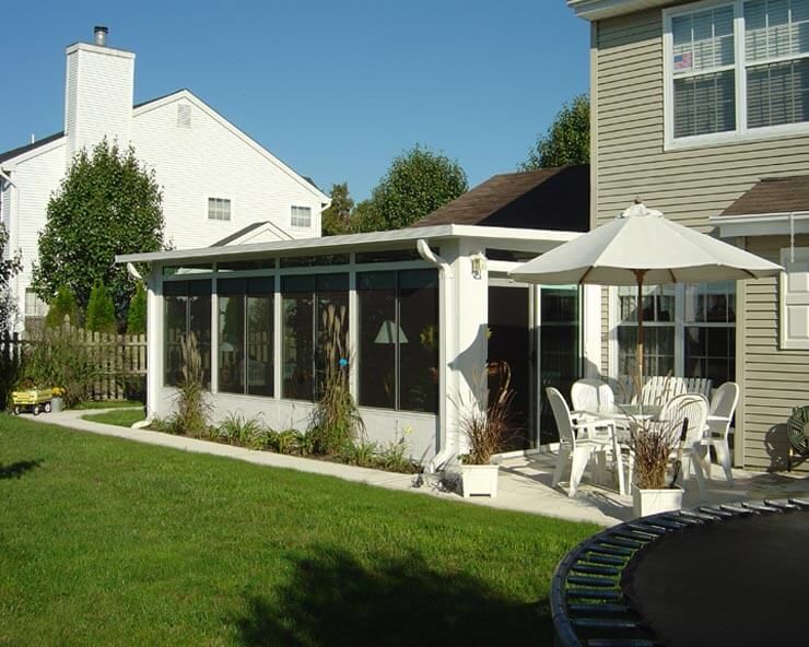 White screened-in patio attached to a beige house, with outdoor furniture and a trampoline.