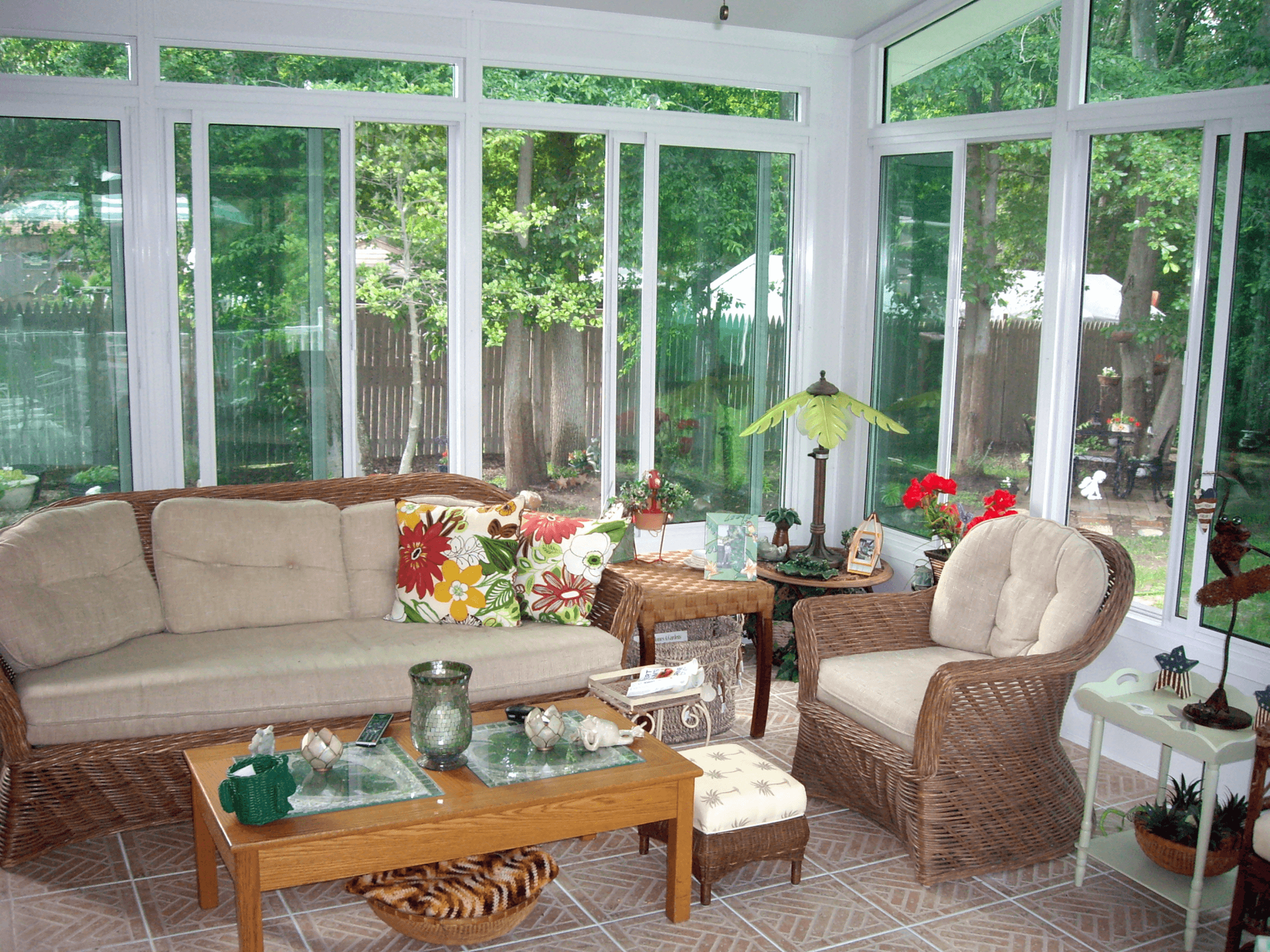 Sunroom with wicker furniture, glass windows, and a view of trees.