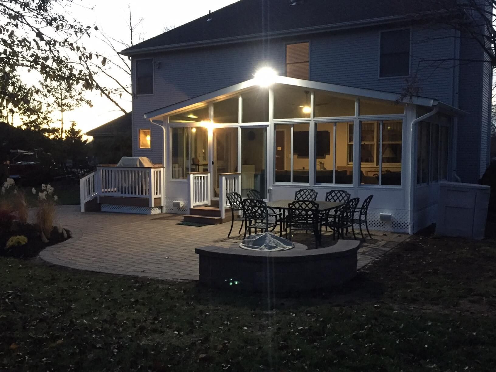 Outdoor patio with a sunroom, fire pit, and a dining set at dusk.