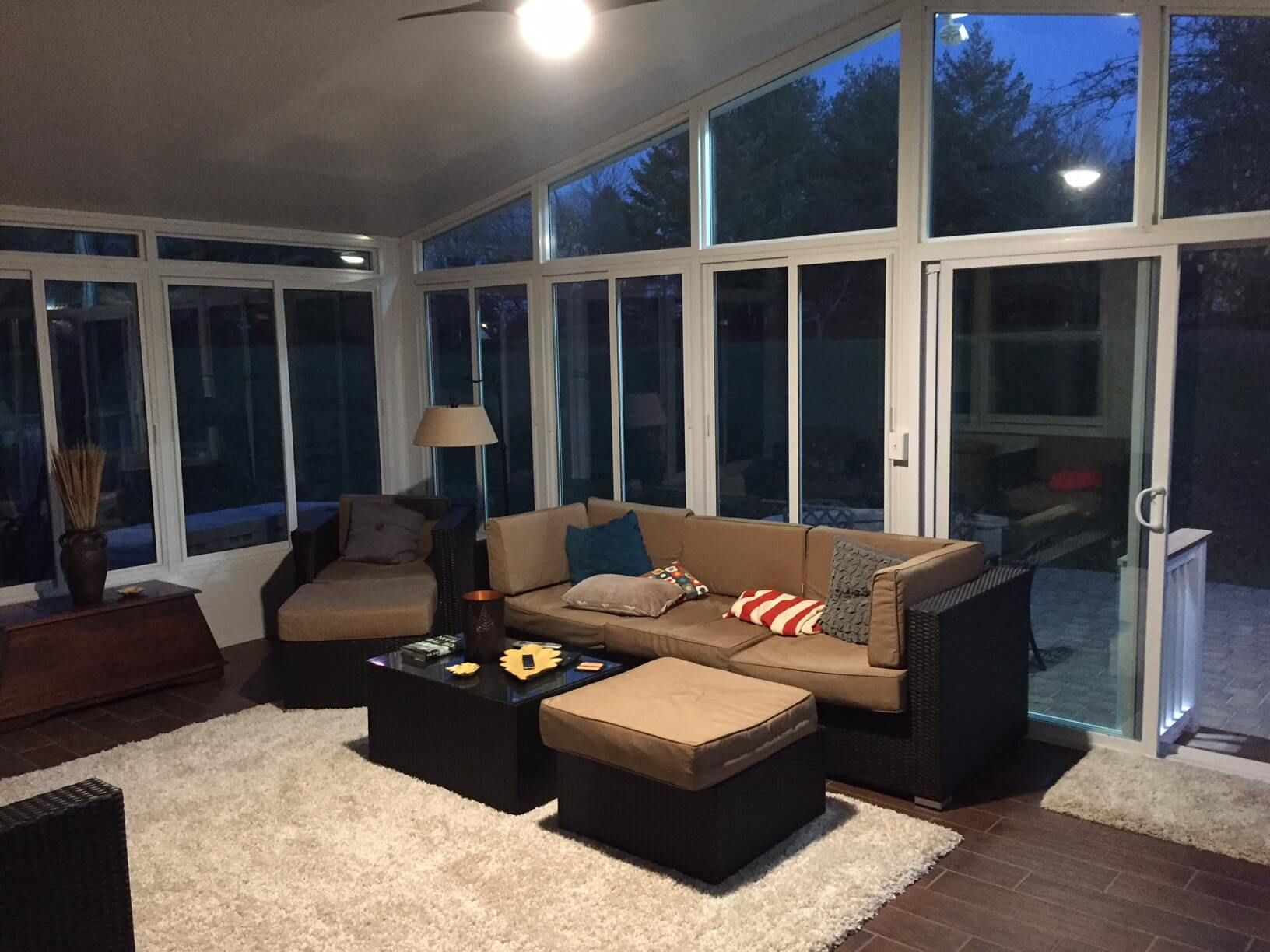 Sunroom with tan couch, ottoman, and large windows looking out at trees.