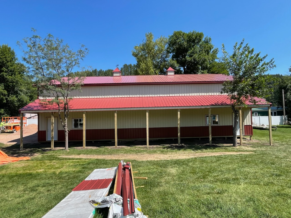 A large white building with a red roof is sitting in the middle of a grassy field.