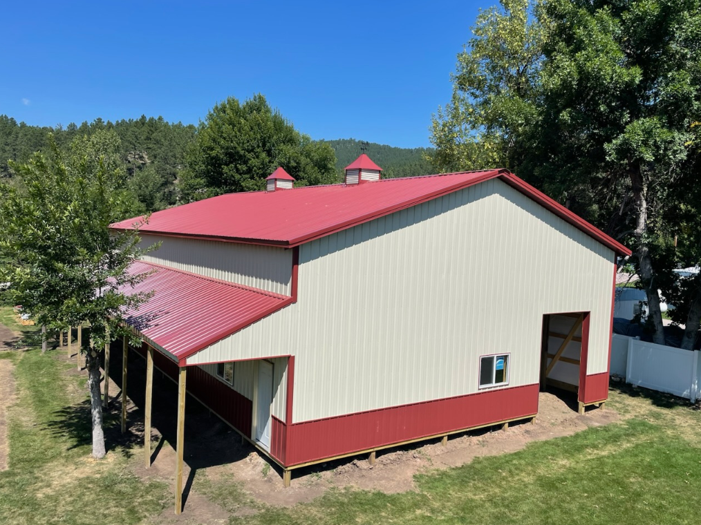 A white barn with a red roof is sitting in the middle of a grassy field.