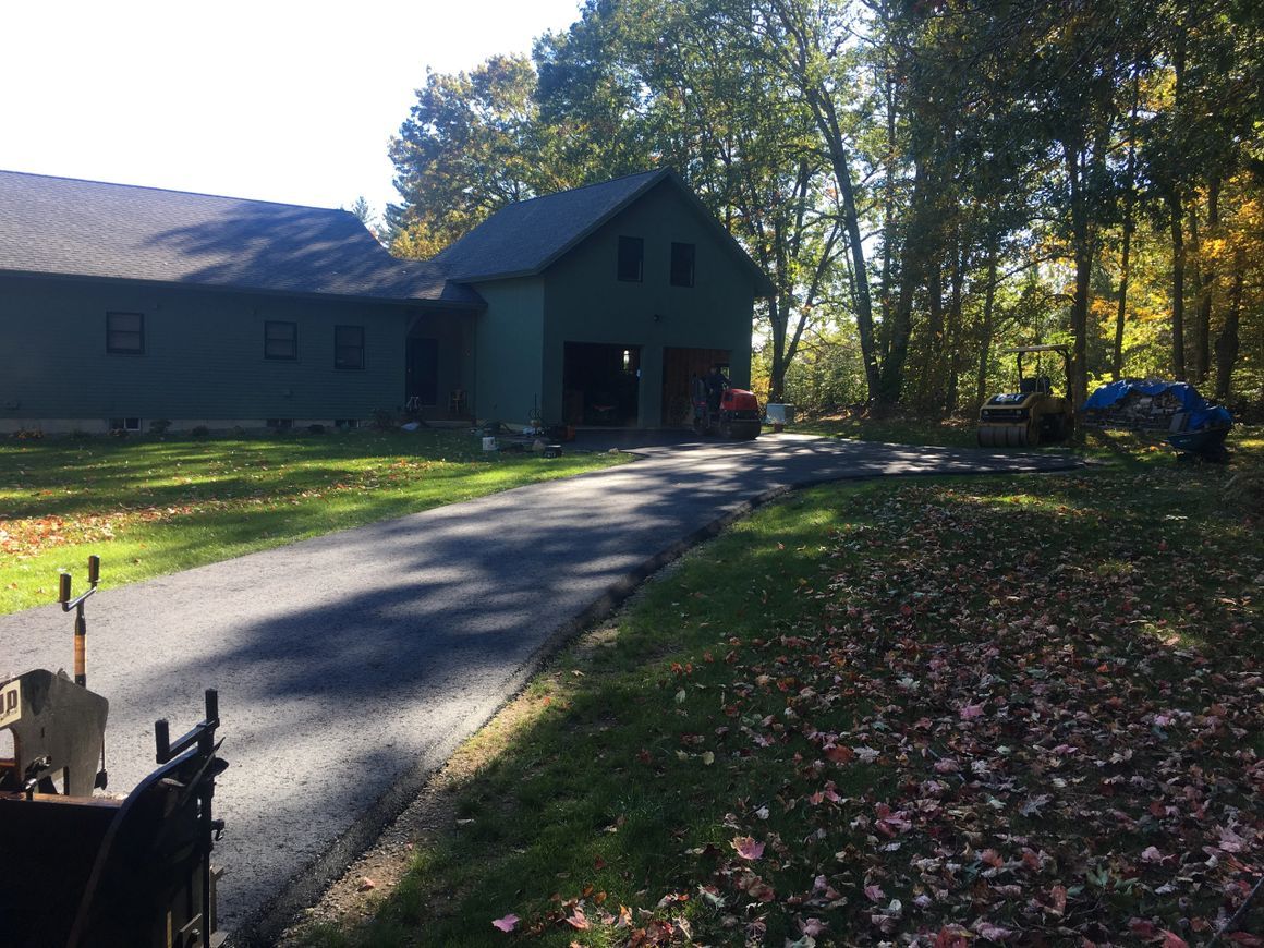 Asphalt driveway leading to a green garage. Autumn leaves and trees surround the property.
