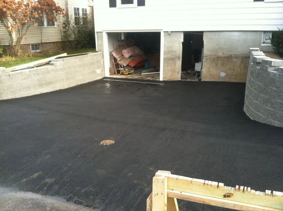 Newly paved asphalt driveway leading to a garage and a retaining wall.