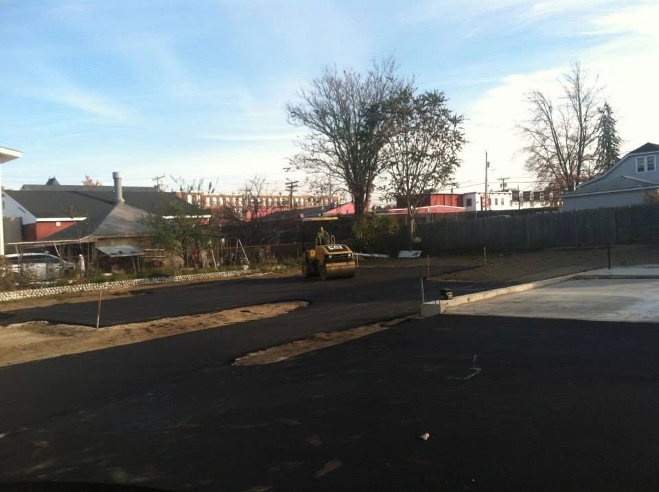 Asphalt paving in progress on a parking lot, with a roller machine compacting the surface.