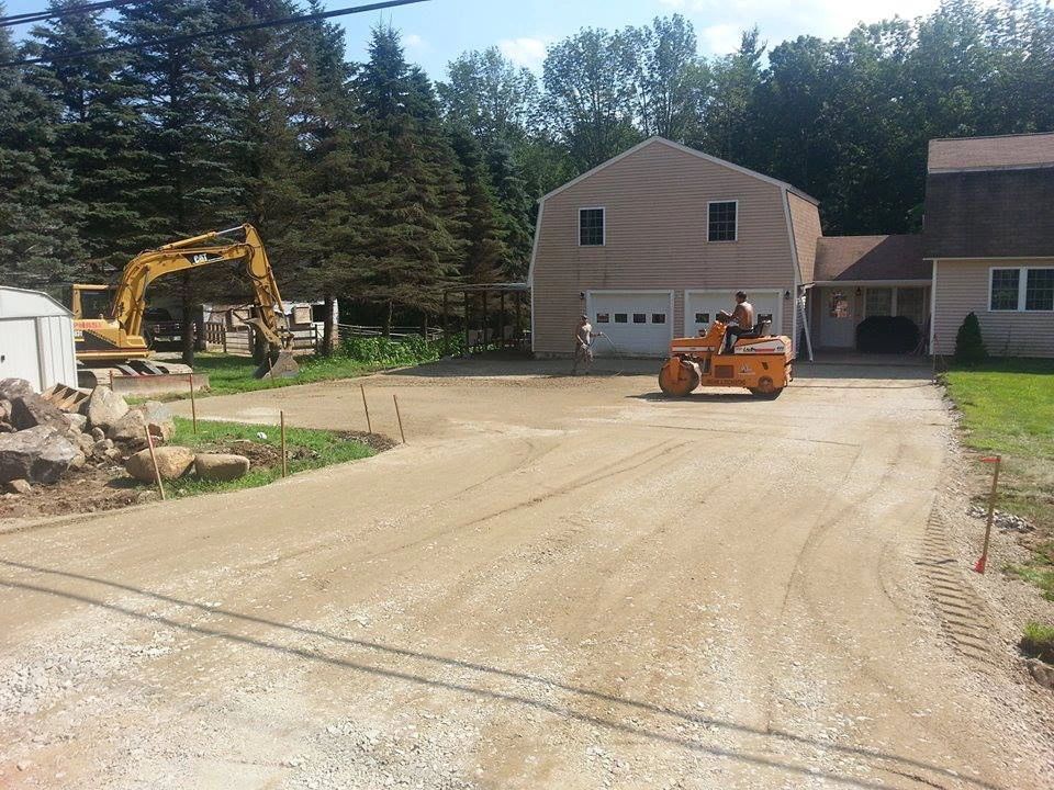 Construction site: gravel driveway being prepared for paving; excavator and roller in use.