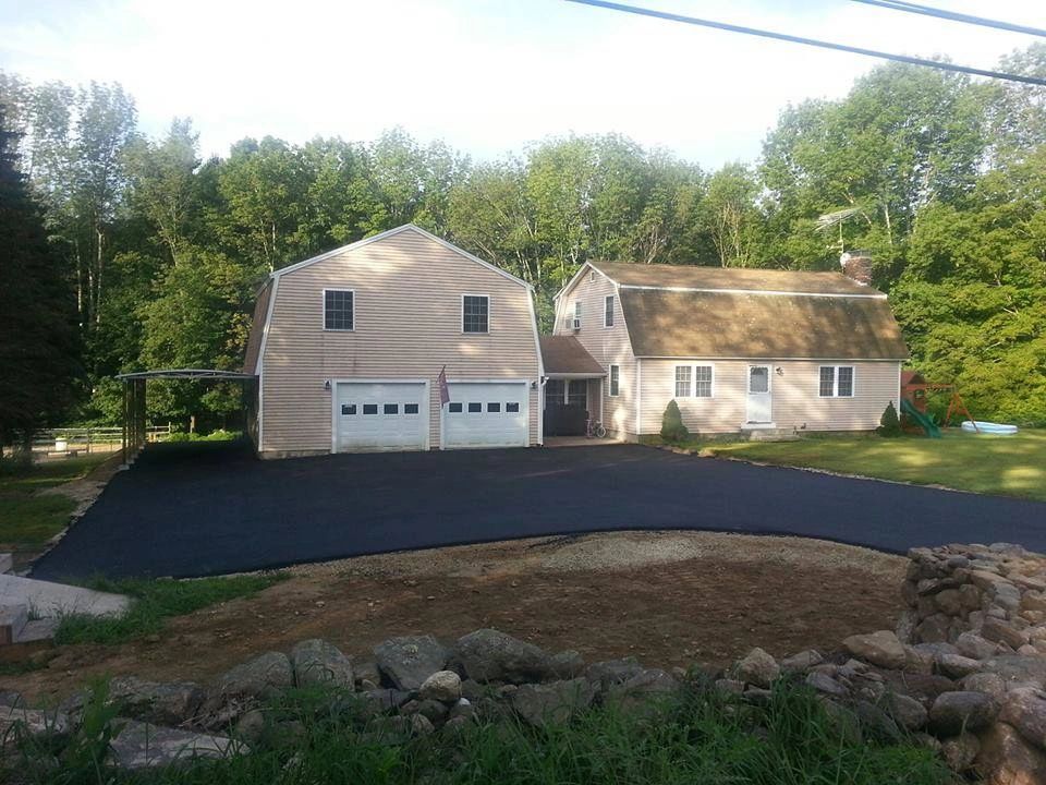 Paved driveway in front of a tan two-story garage and house, surrounded by trees.