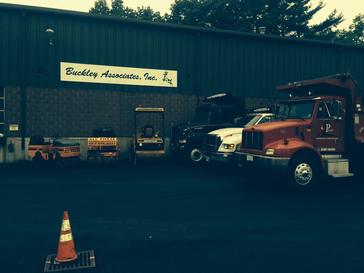 A business exterior, Buckley Associates, with trucks, equipment, and an orange traffic cone.