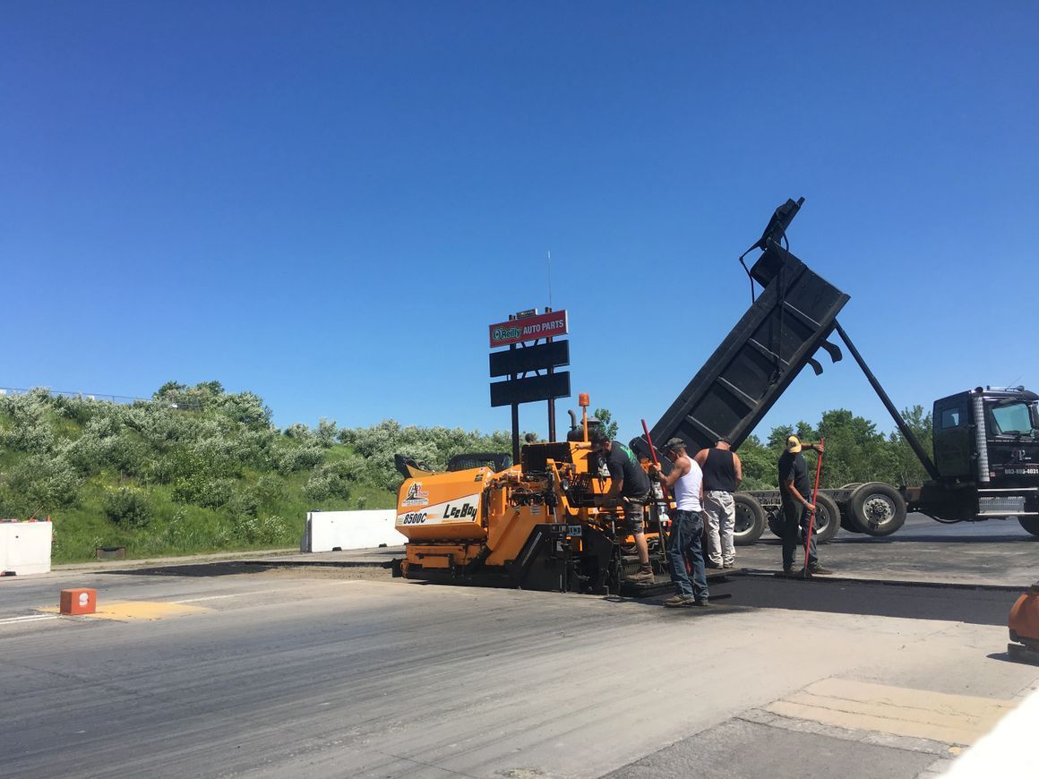 Asphalt paving in progress: asphalt paver receiving material from a dump truck under a blue sky.