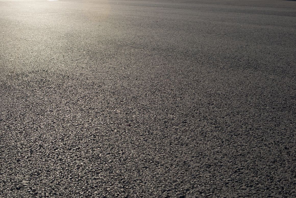 Close-up view of freshly paved asphalt road, textured and dark gray with sunlight reflecting.