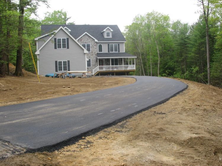 Two-story house with a long, curved asphalt driveway and a wooded backdrop.