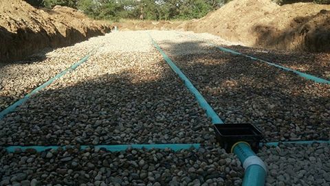 Gravel-filled trench with blue pipes, part of a septic system installation.