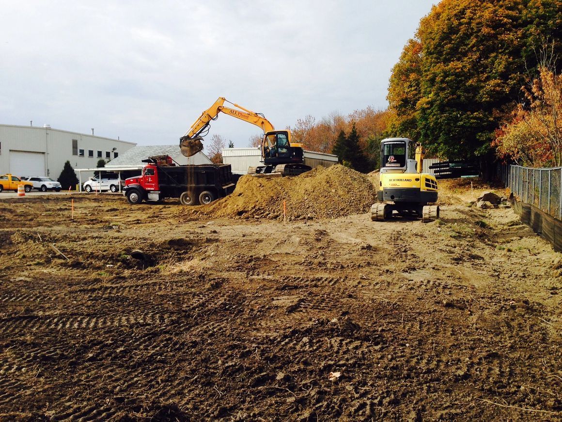 Construction site with excavator loading a dump truck. A smaller excavator also works nearby.