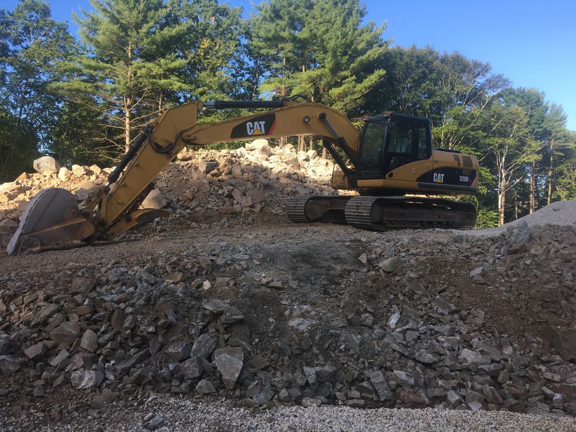Yellow Caterpillar excavator on a pile of rocks. Trees in the background.