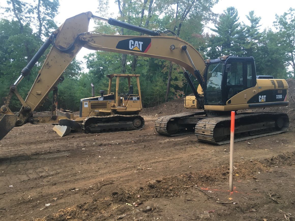 Two CAT construction vehicles on a dirt construction site; one with a digging arm, the other a smaller bulldozer.