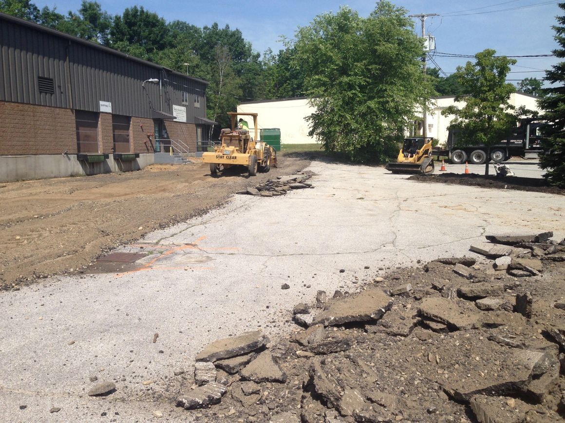 Construction site with two bulldozers, partially demolished asphalt, and a building on a sunny day.