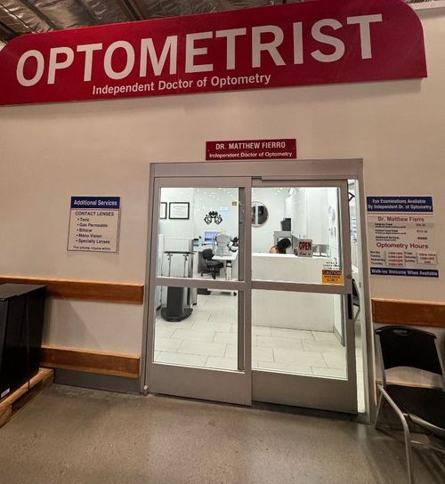 Optometrist office entrance with red sign, glass double doors, and seating in a hallway.