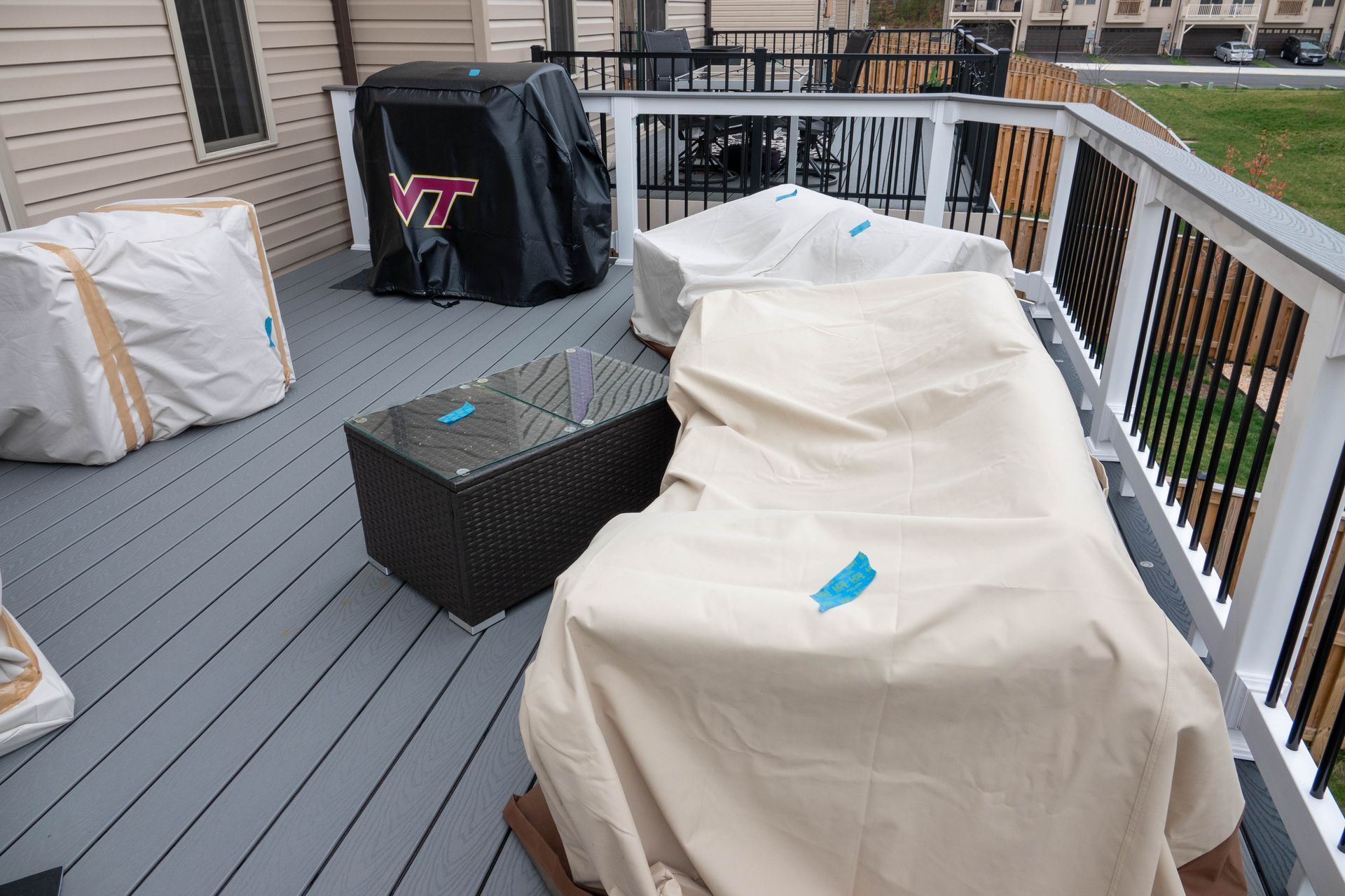 Deck with covered furniture. Grill with VT logo. Gray deck boards and white railing.
