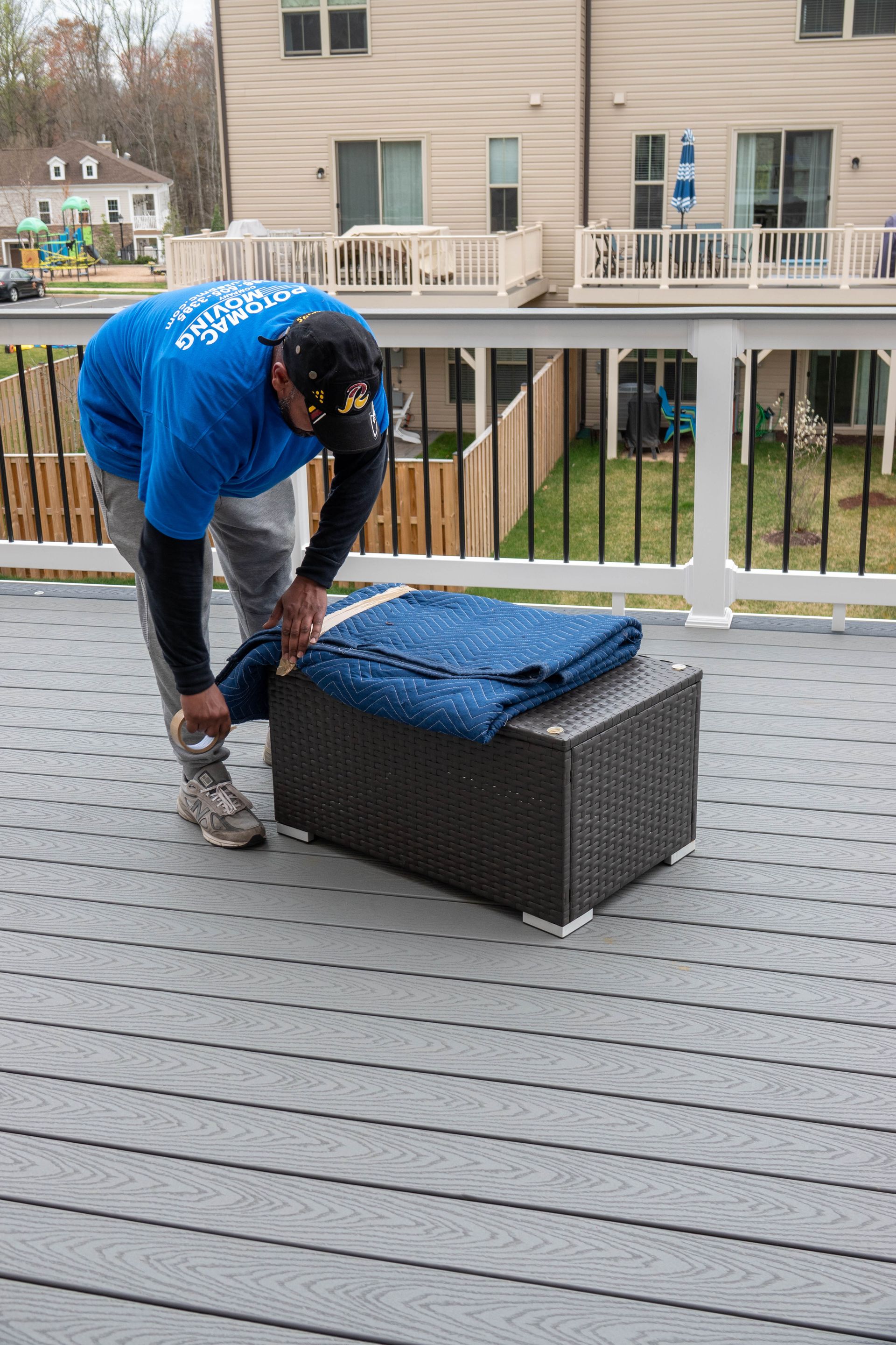 Person on a deck tying something on a dark wicker ottoman. Blue blanket on top.