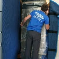 Man in blue shirt working with wrapped furniture.