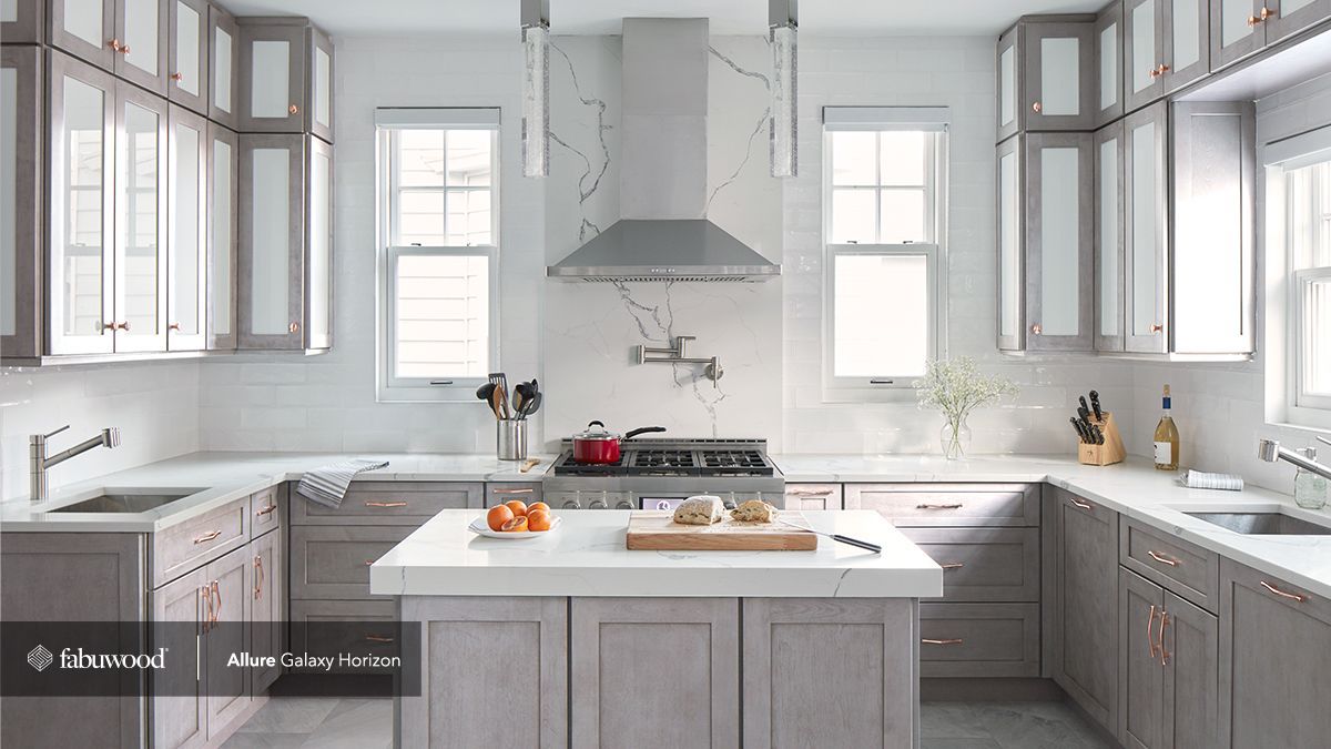 A kitchen with gray cabinets, white countertops, and a large island in the middle.