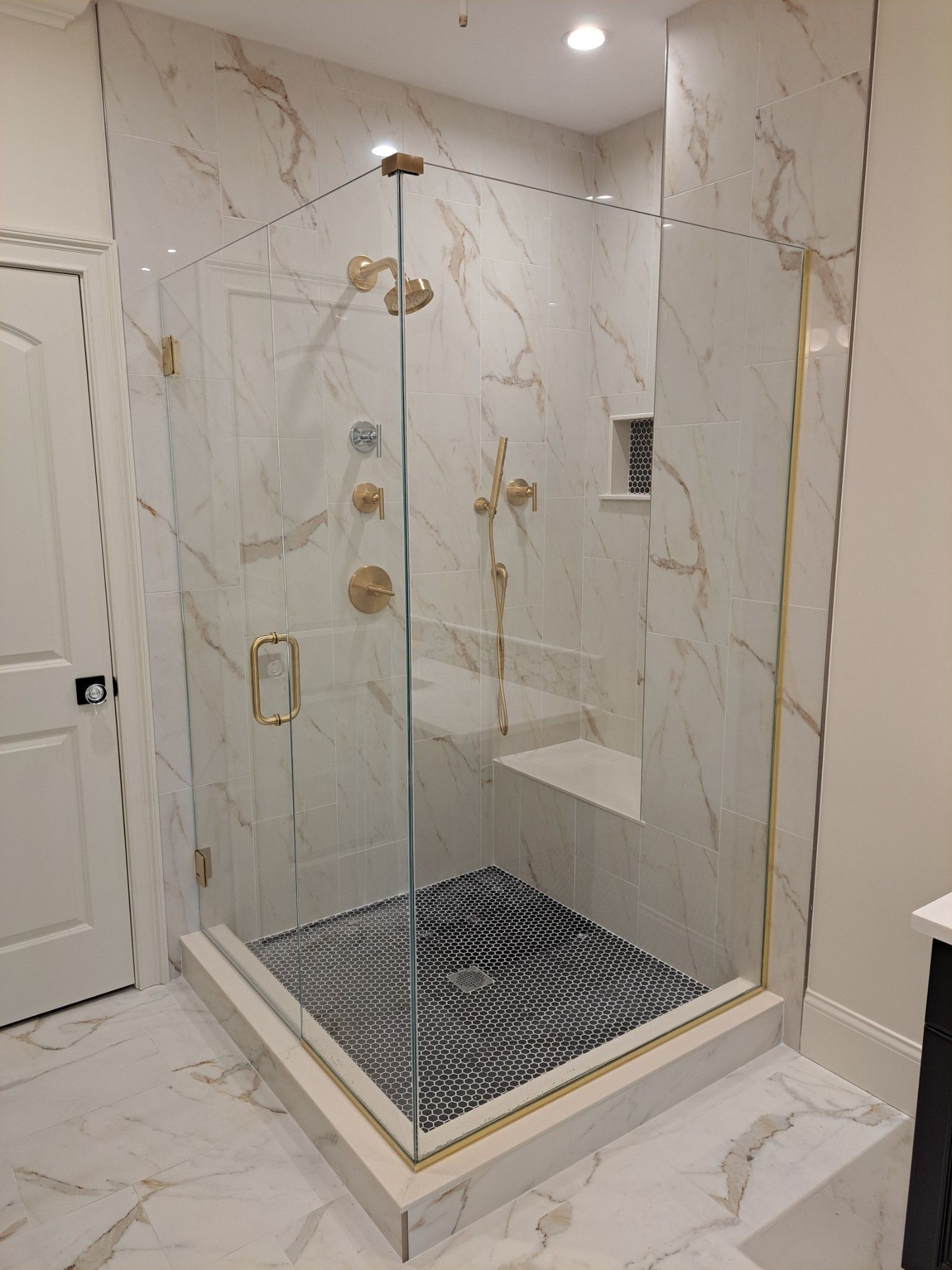 A bathroom with marble tiles and a walk in shower with a glass door.