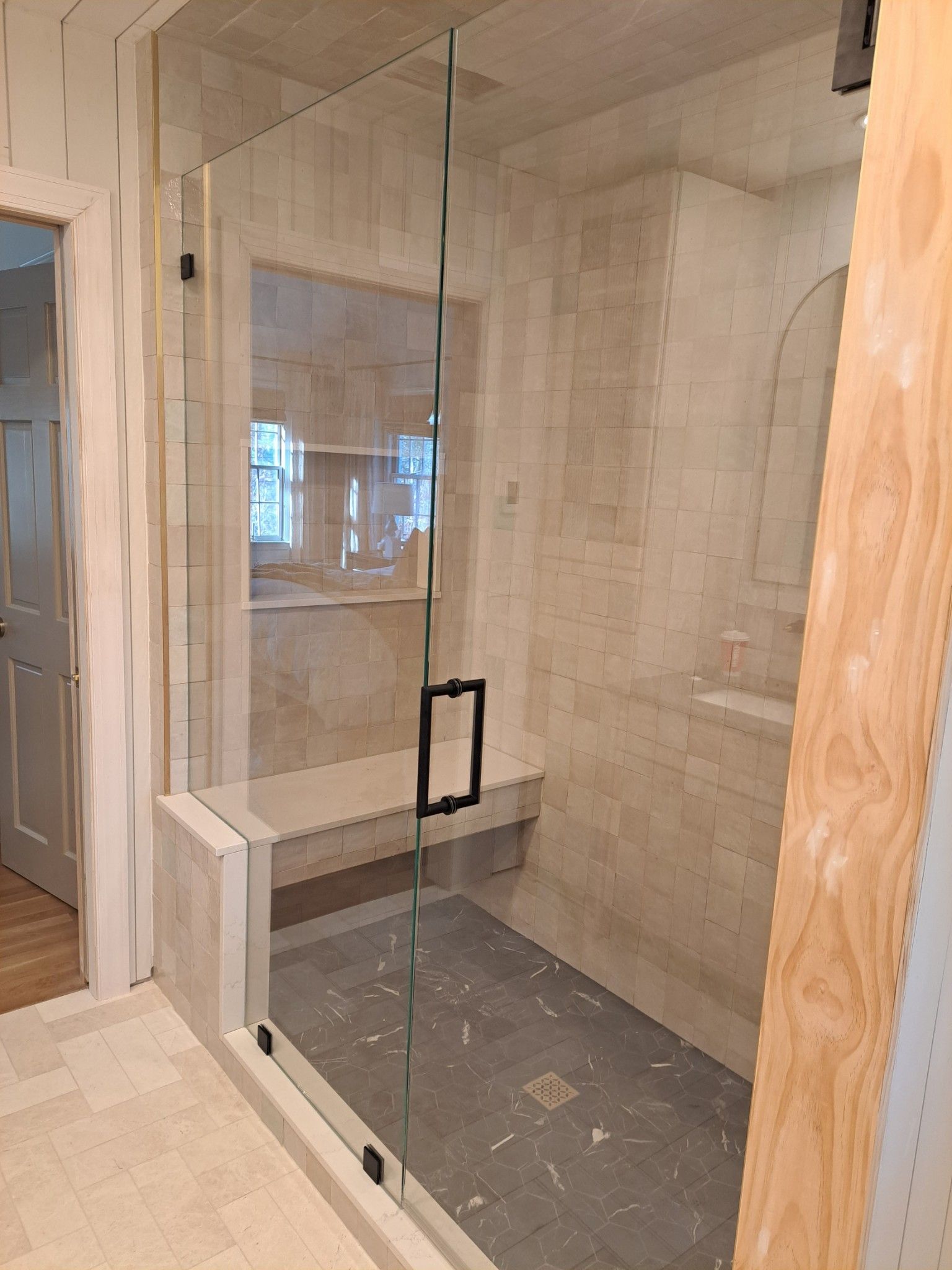 A bathroom with a glass shower door and a bench.