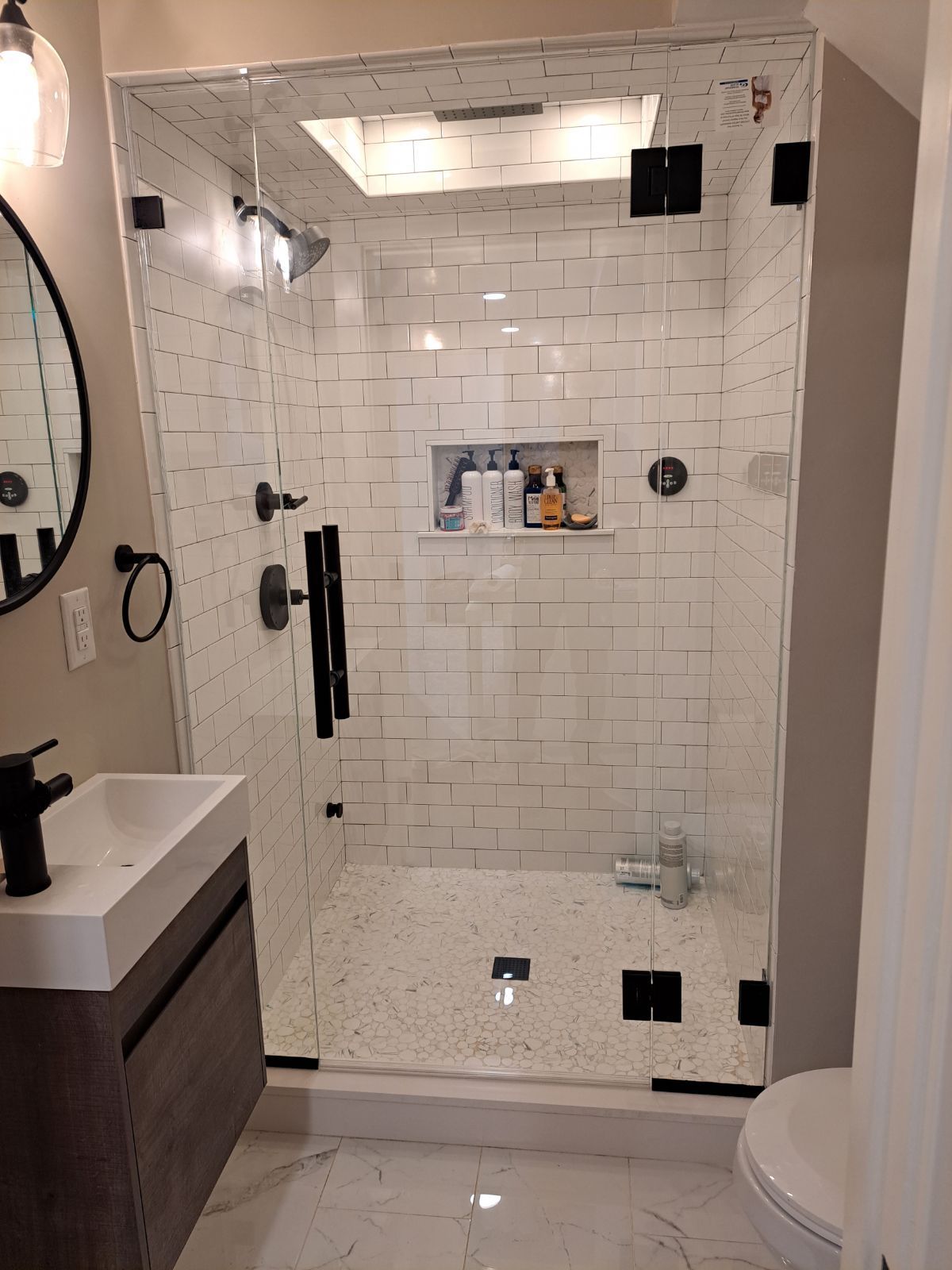 A bathroom with a walk in shower , sink , toilet and mirror.