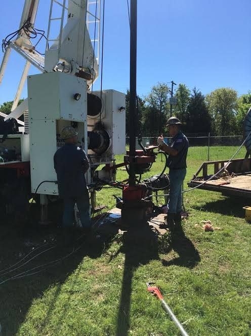 Two workers near a drilling rig on a grassy field on a sunny day.