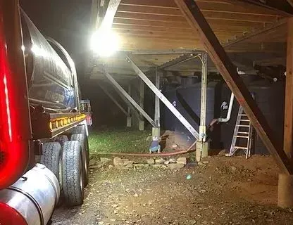 Truck filling water tanks under a wooden structure at night.