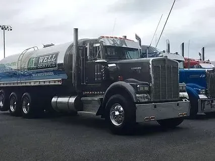 Black tanker truck with chrome accents, parked in a lot. The tank has blue and green graphics.