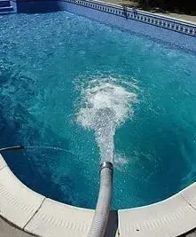 A pool with a hose expelling water, creating a foamy disturbance in the clear, blue water.
