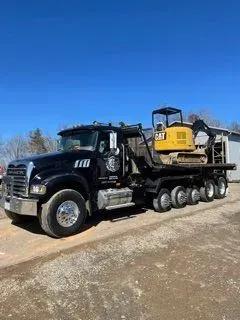 Black Mack truck transporting a yellow Caterpillar excavator on a flatbed trailer, outdoors.