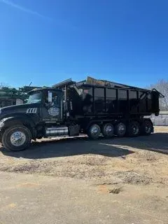 Black dump truck under a blue sky, parked on a paved lot.