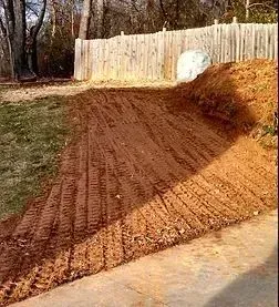 Dirt ramp with tire tracks, leading up to a wooden fence. Ground is brown, setting is outdoors.