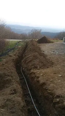 A trench dug in dirt with a white pipe running through it, mountains in the background.