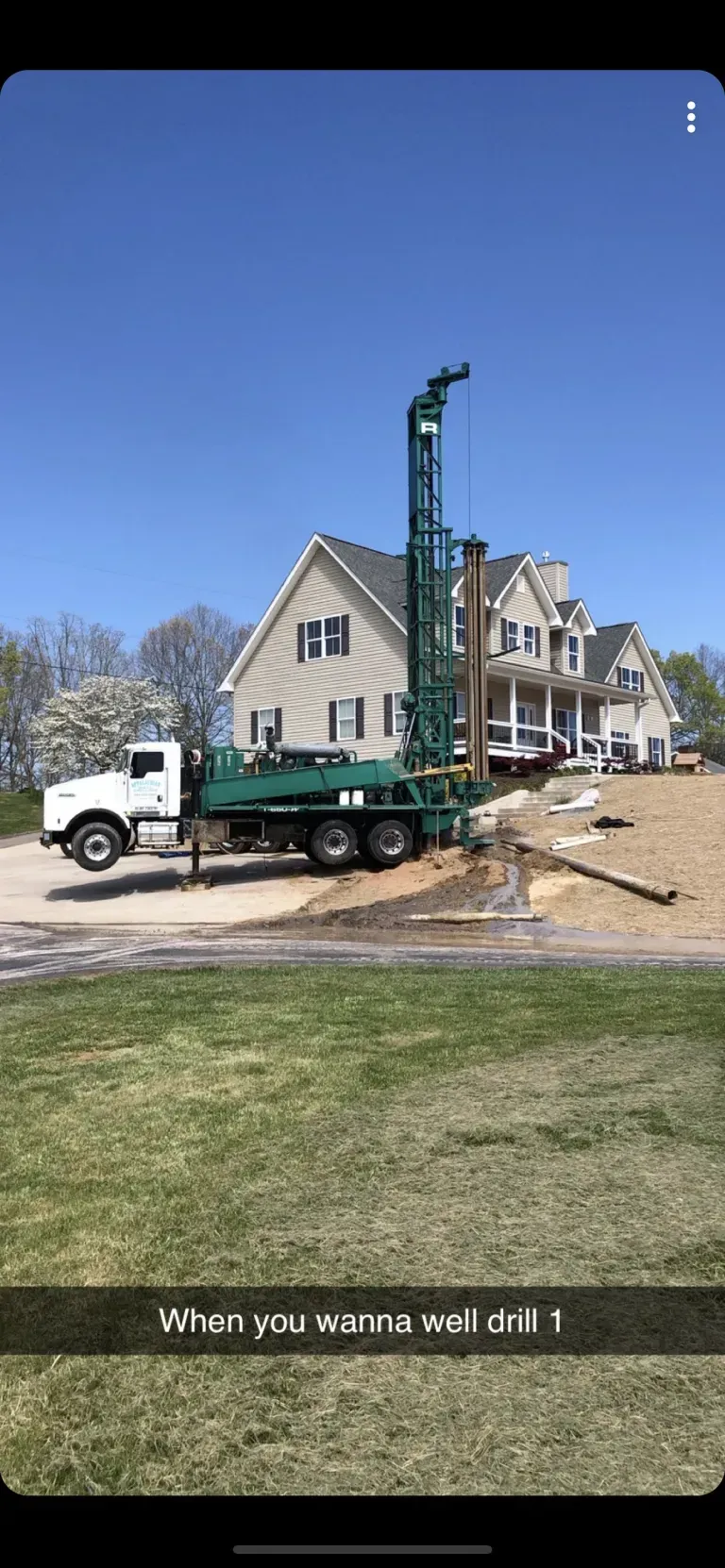 Drilling rig in front of a house, bright blue sky, and a grassy area.