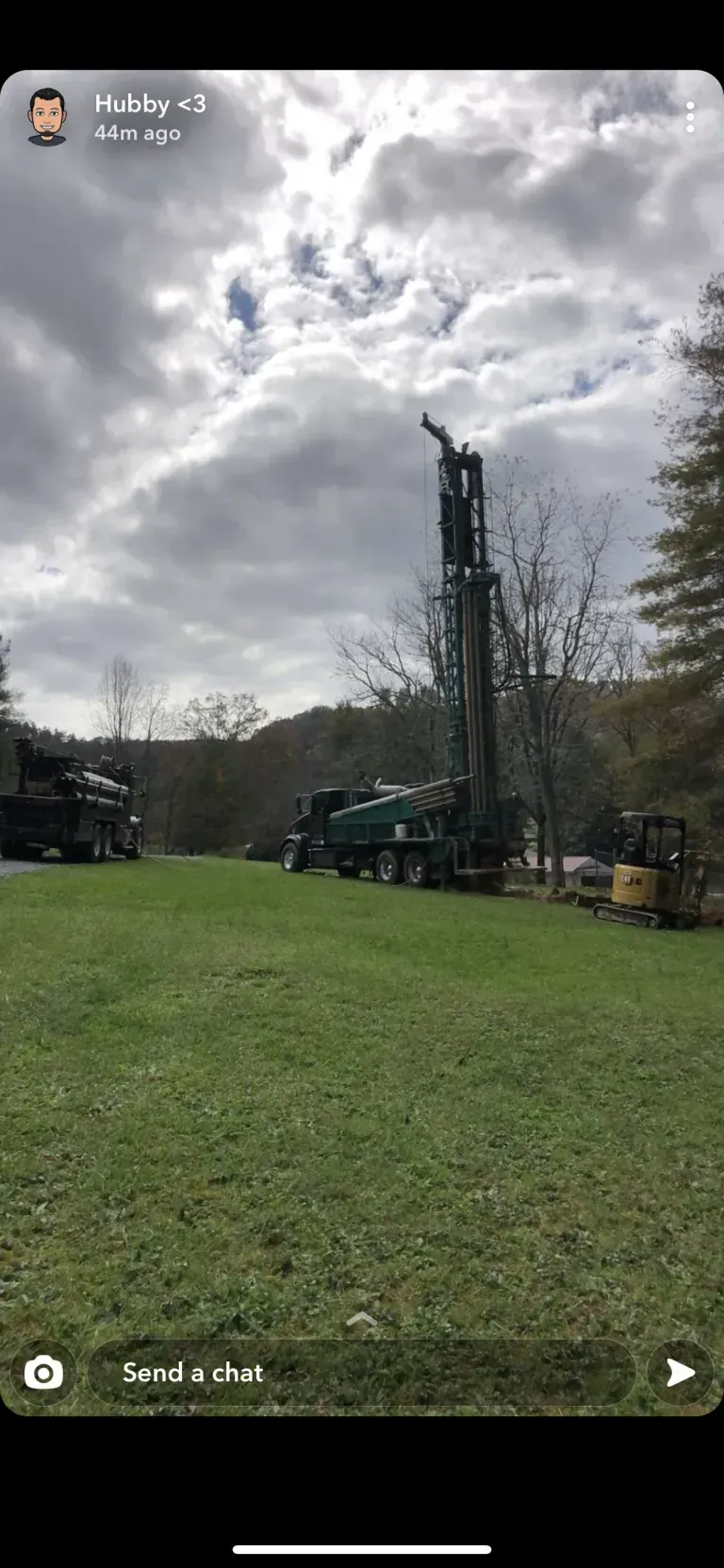 A drilling rig and trucks on a grassy field under a cloudy sky.