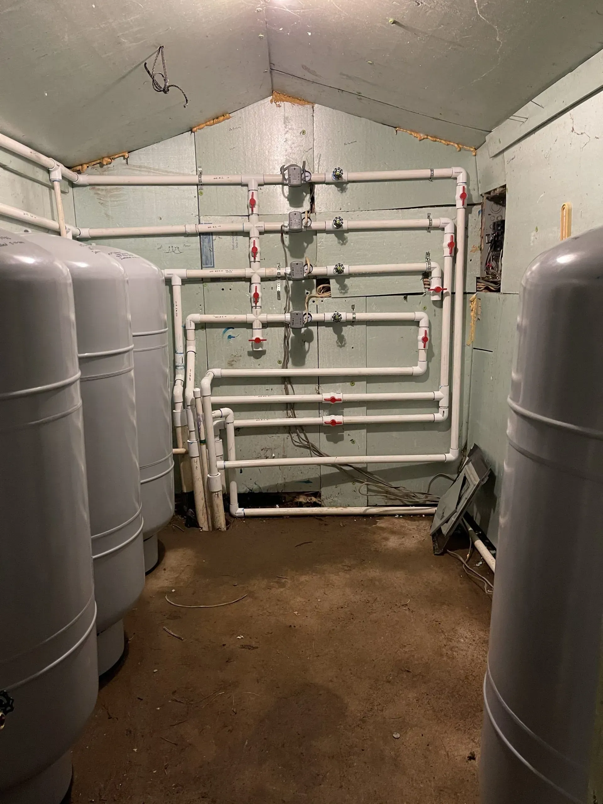 A room with water tanks and white pipes. Dirty floor and green walls.
