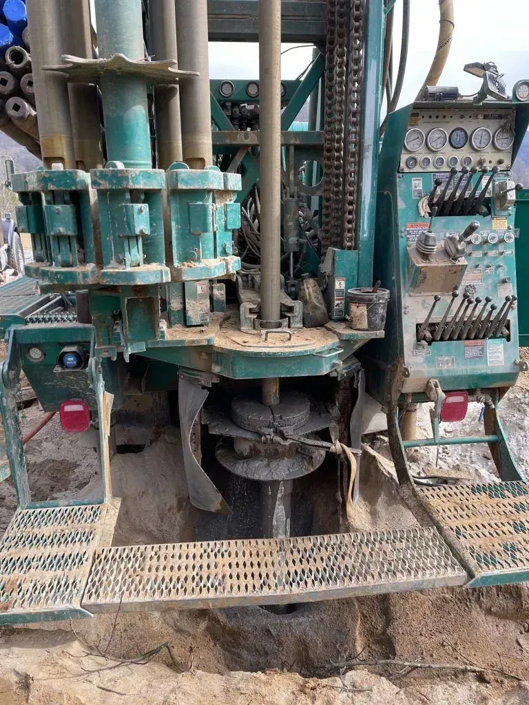 Green drilling rig boring into the earth. Metal equipment with gauges and chains.