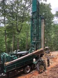 Well drilling rig in a wooded area, drilling into the earth. Green machine, tree backdrop.