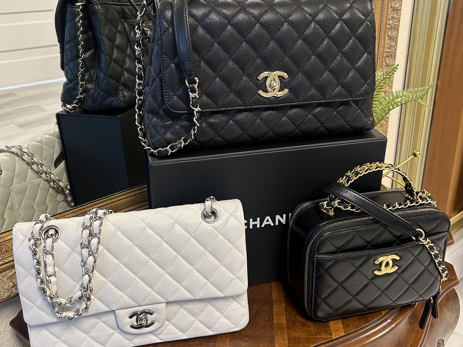 Three Chanel handbags, two large quilted bags in black and white and one smaller black vanity bag, on a box and table.