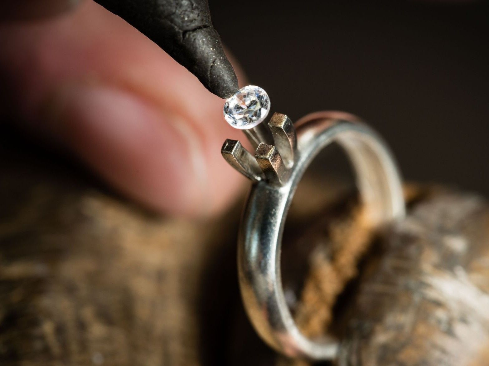 A jeweler uses a tool to carefully place a small, sparkling gemstone into the prong setting of a silver ring.