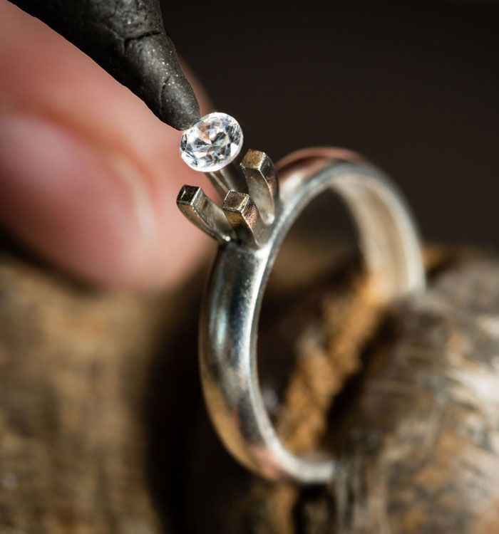 A person is working on a ring with a diamond in it.