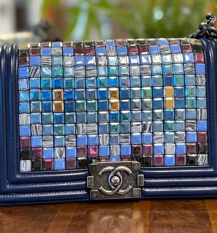 A blue purse with a mosaic pattern is sitting on a wooden table.
