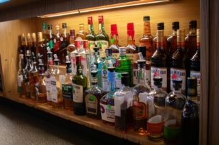 Bar shelf lined with various liquor bottles under a light.