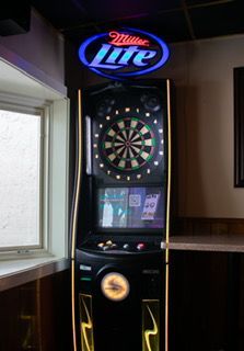Dartboard machine with Miller Lite sign above, near a window and bar.