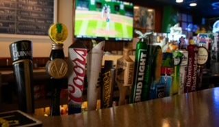 Beer taps on a bar; a TV screen shows a sports game in the background.